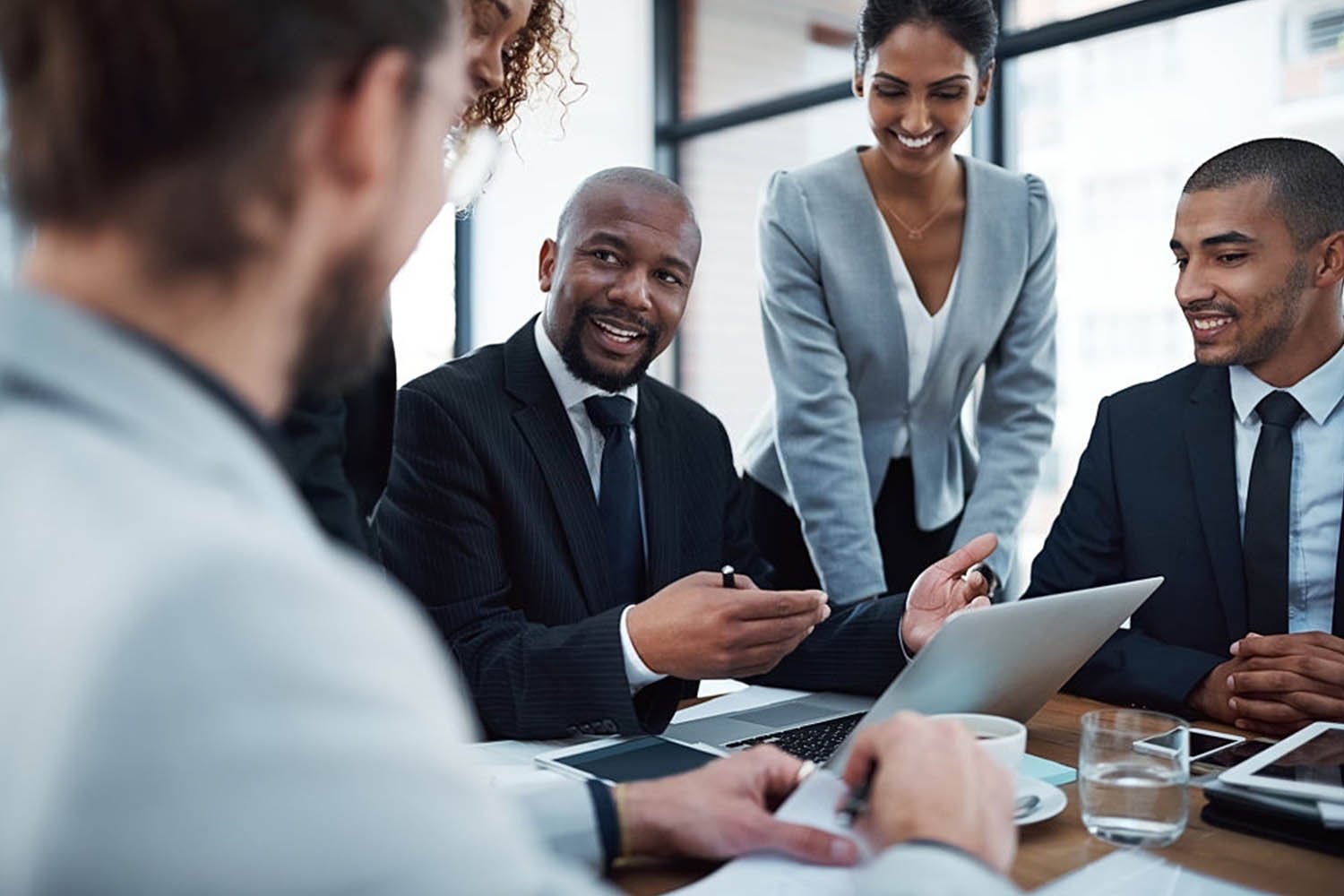 Group of five diverse professionals having a business meeting in a modern office with large windows.