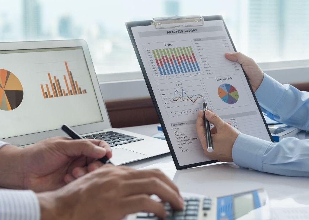 People analyzing business data with charts and graphs on a tablet, laptop, and clipboard.