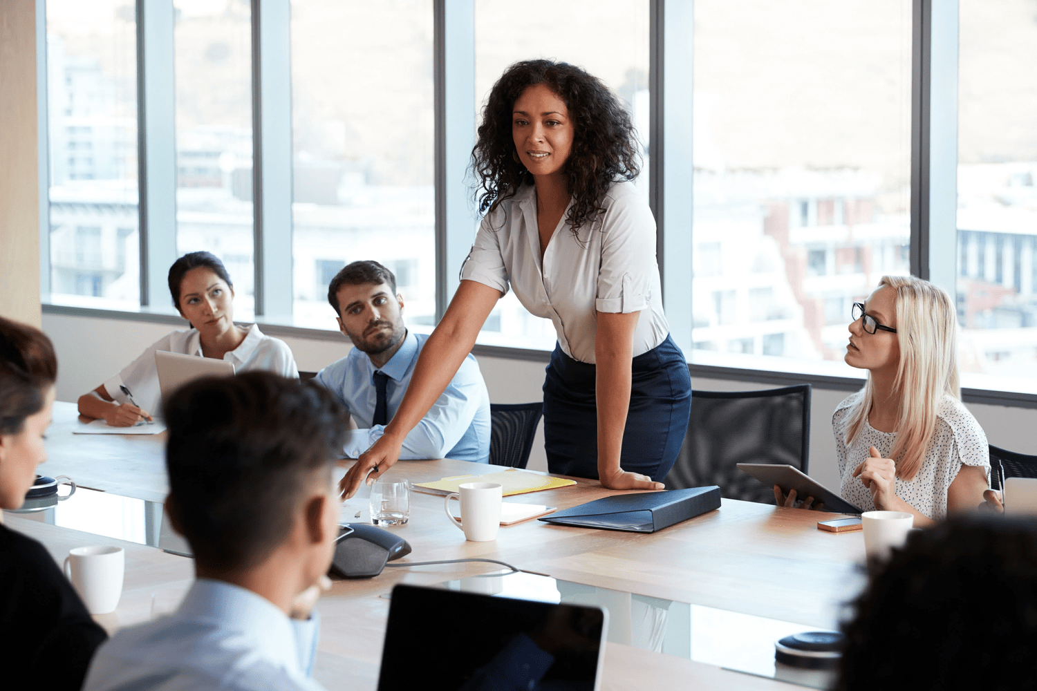 A woman standing at a conference table speaking to a group of people.