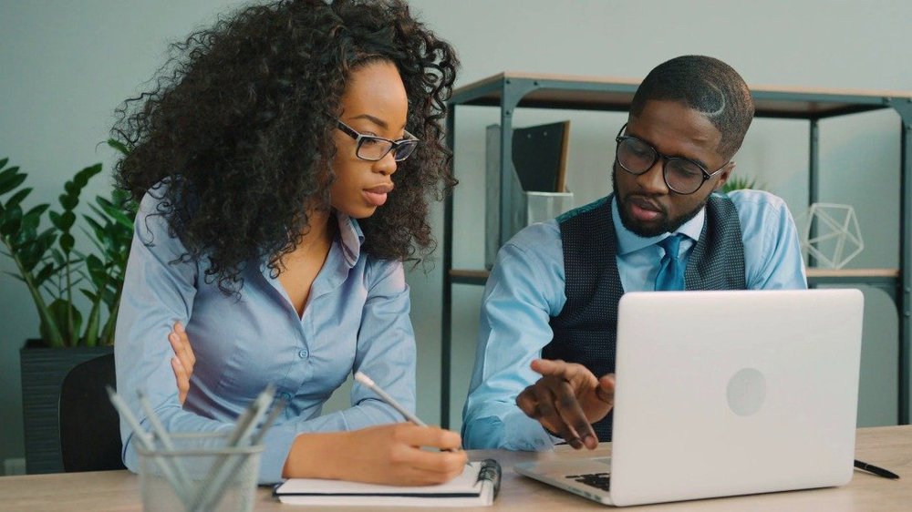 Two professionals working together at a desk with a laptop.